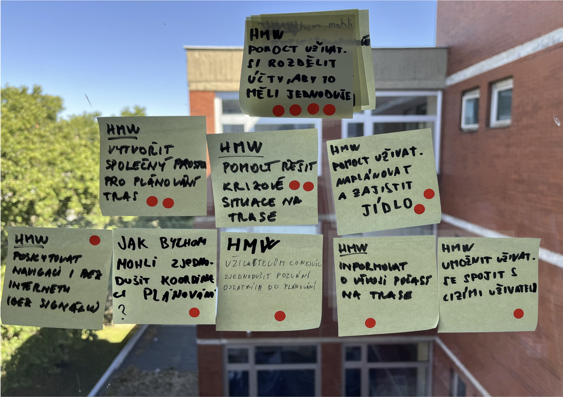 Fotka post-itů s HMW otázkami nalepených na okně — výstup týmového brainstormingu